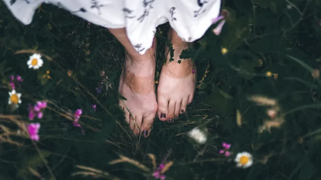 A person practicing sensory roaming in minimalist hiking shoes, feeling the textured moss of the forest floor.