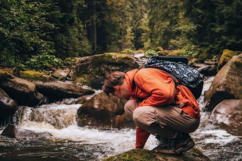 hiker Squatting at a clear backcountry stream, filtering water from a soft flask in golden hour light, embodying wu wei