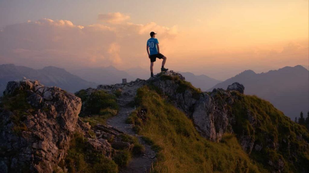 A lone hiker standing on a high ridge at dusk, the peak behind them already climbed, practicing Daoist knowing when to stop — the descent ahead through fading light