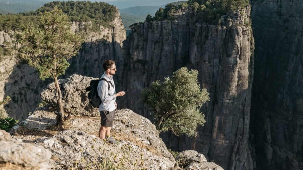 A hiker in a UPF sun protection shirt standing on a sunny ridge, the shirt light and breathable, the sun behind them casting a long shadow