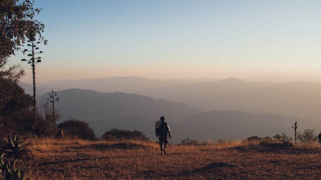 return of the trail - A solo backpacker walking DOWN a winding rocky mountain trail at golden hour dusk, misty pine mountain valley in the distance, quiet mood, aesthetic tones, muted colors, authentic backcountry photography