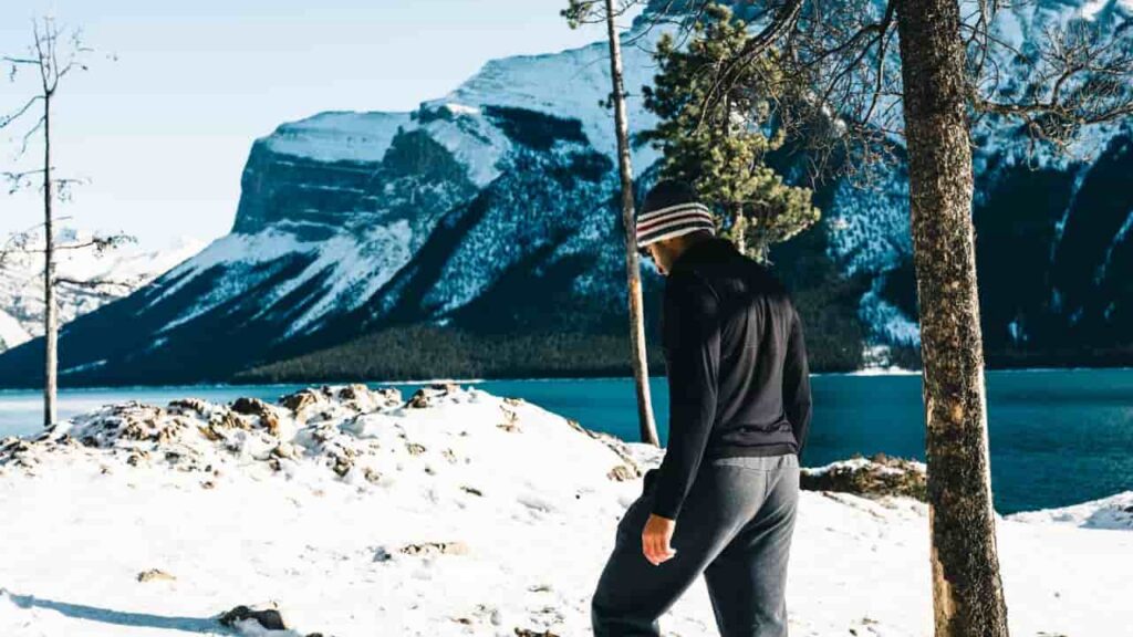 hiking base layer for cold weather - A hiker adjusting a merino wool base layer at a mountain camp, the base layer close to the skin and quiet, doing the work of thermoregulation without being noticed