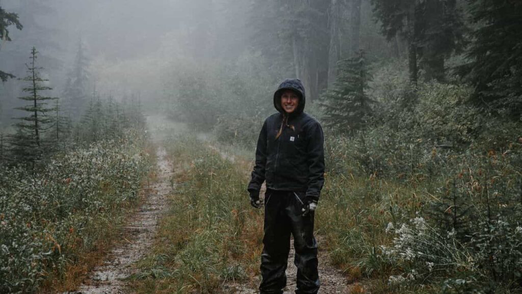 A hiker walks through the mountain forest in the rain, wearing waterproof hiking trousers over their hiking boots.