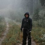 A hiker walks through the mountain forest in the rain, wearing waterproof hiking trousers over their hiking boots.