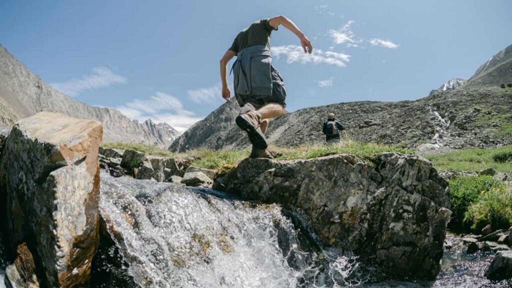 hiking shorts - A hiker in shorts and hiking boots crossing a stream on a summer trail